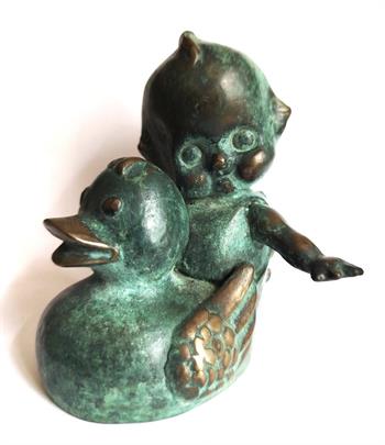 Bronze sculpture of a Kewpie doll riding a toy duck with a green verdigris patina, titled Voyage by Grace Kotze.