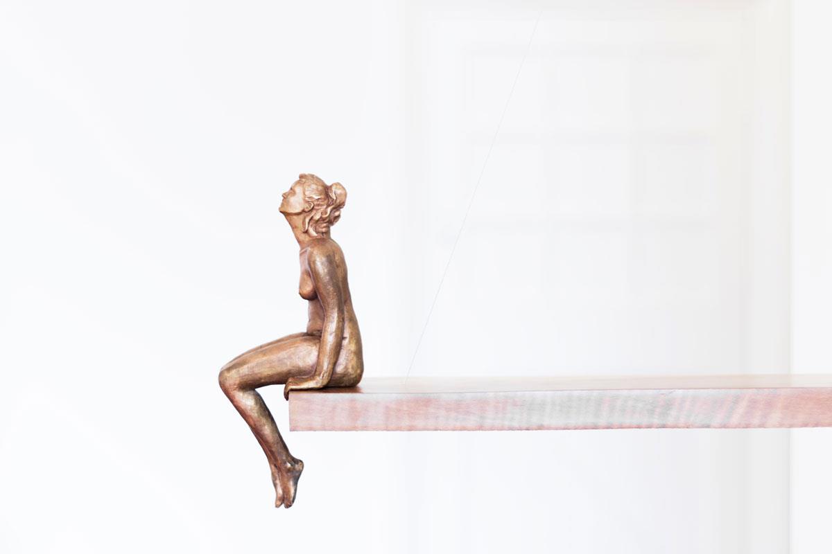 bronze sculpture of a nude woman seated on a diving board