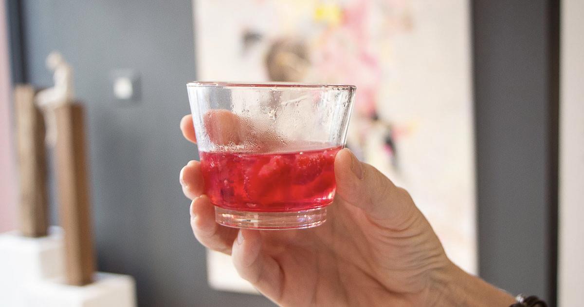 A hand holding a small glass of red gin