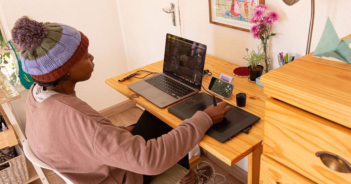 Balekane Legoabe at her desk working on digital artworks using a laptop and drawing tablet.