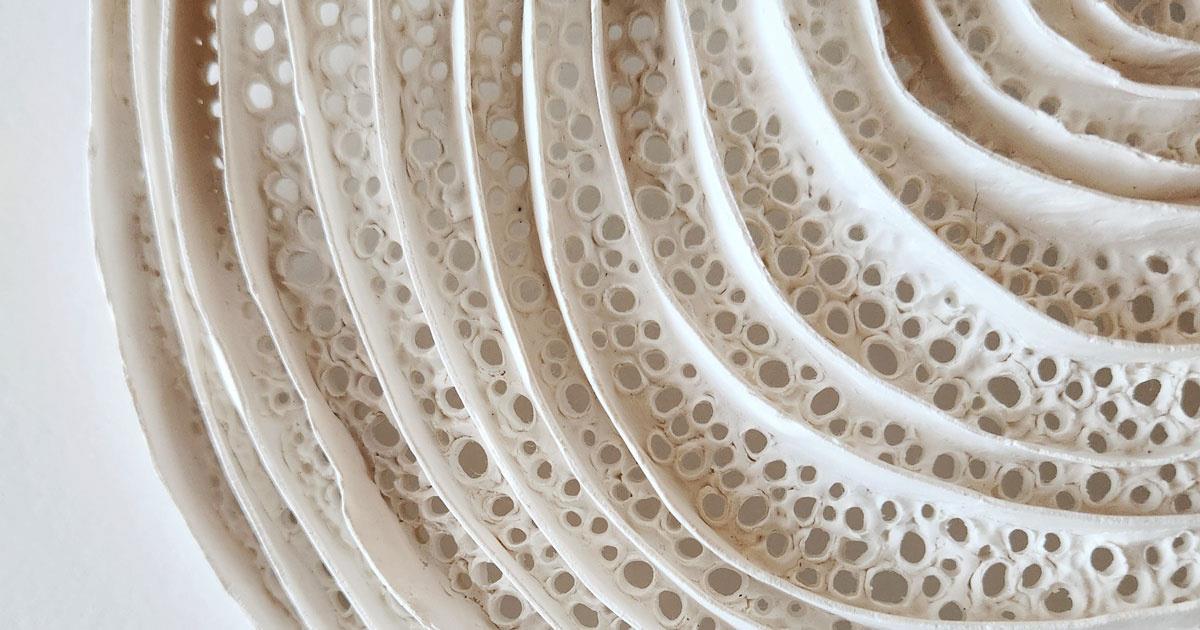 Close up detail of Jo Roets' clay sculpture art depicting multiple rings, like a tree stump, and the bottom of the clay is perforated with multiple mismatched holes.