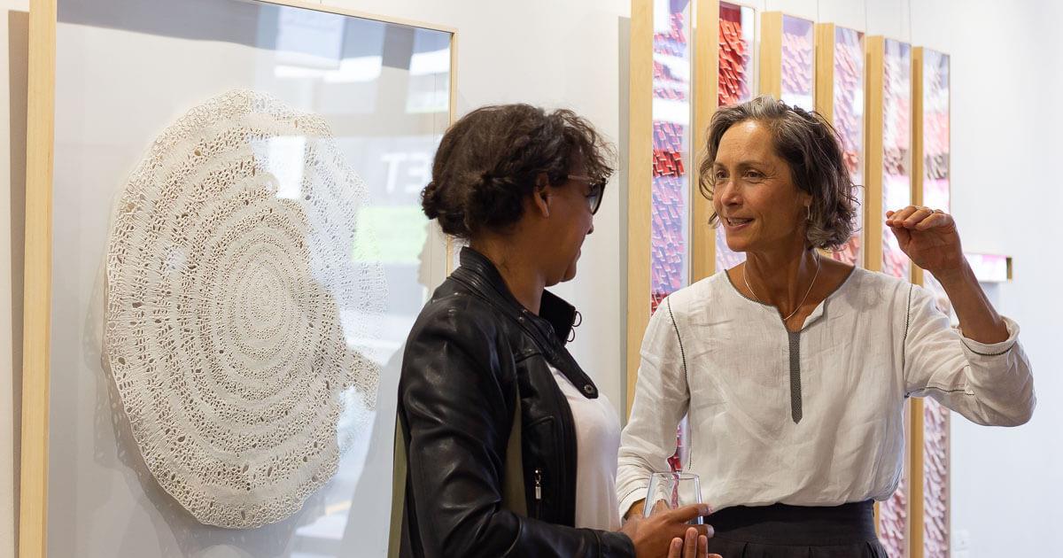 Catherine Ocholla and Lisette Forsyth are in conversation in front of artwork by Jo Roets and Karla Nixon