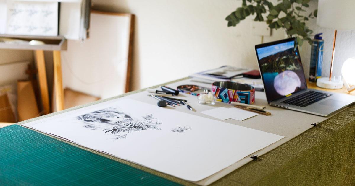 A pencil drawing of a monkey by Kendall-Leigh Nash on her desk in her studio, artist materials in the background.