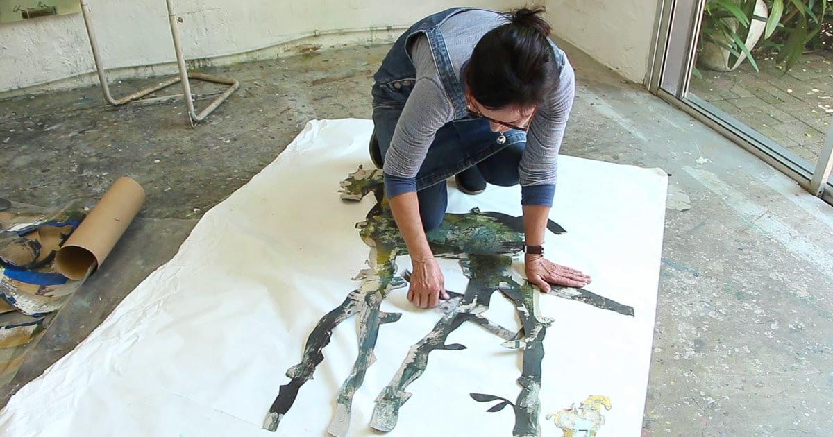 Pascale Chandler arranges a stencil of a long legged horse on top of a canvas